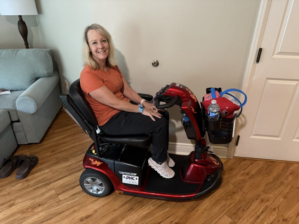 Nancy seated on her mobility scooter inside a Disney World resort room, preparing for a day in the parks.