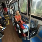 Nancy seated on her mobility scooter inside a Disney World bus, smiling and ready to explore the parks.