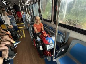 Nancy seated on her mobility scooter inside a Disney World bus, smiling and ready to explore the parks.