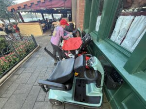 Nancy standing behind her scooter among several others at Disney, highlighting real-life visibility challenges for senior guests.